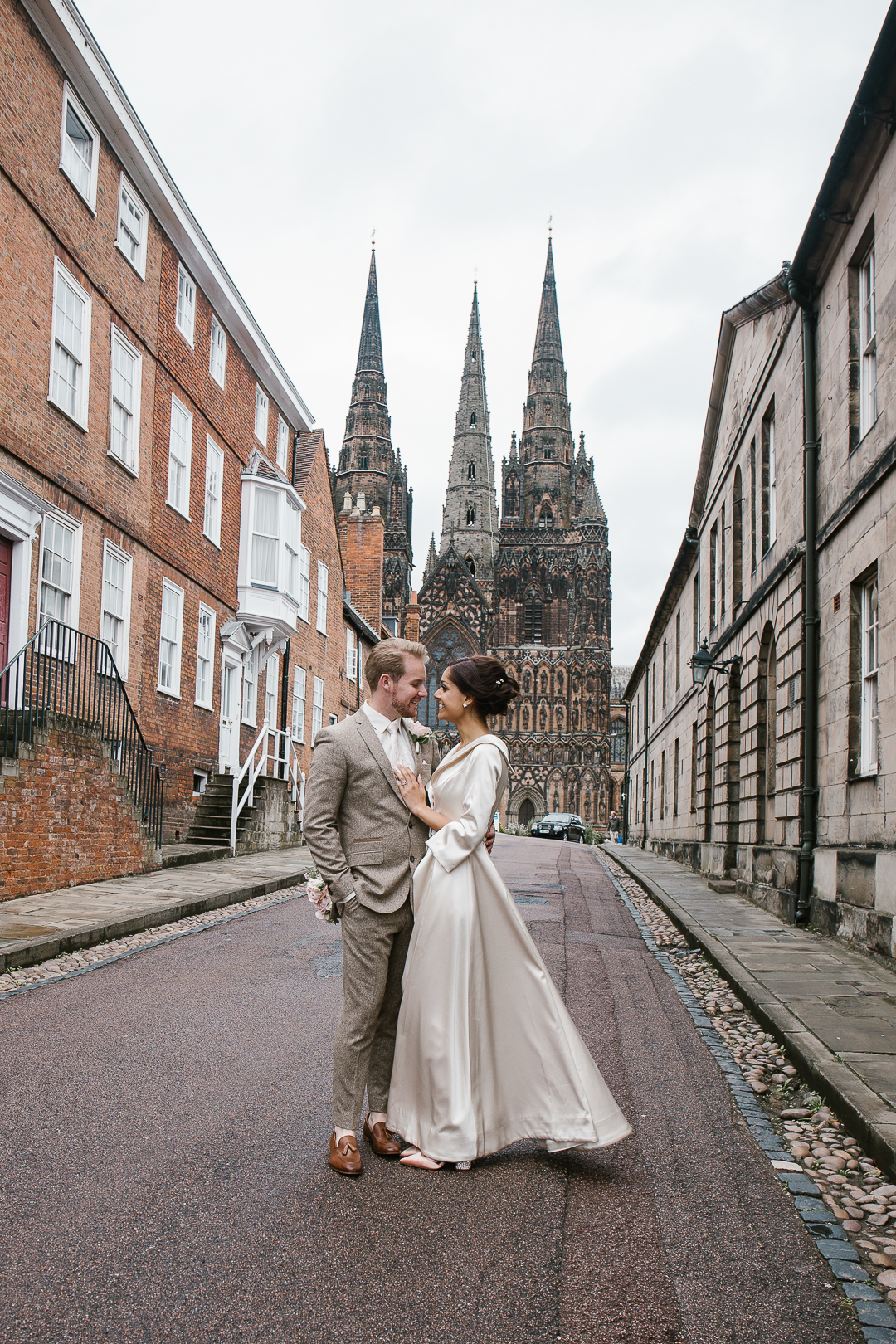 romantic photo of bride and groom smiling at one another with lichfield cathedral in the background