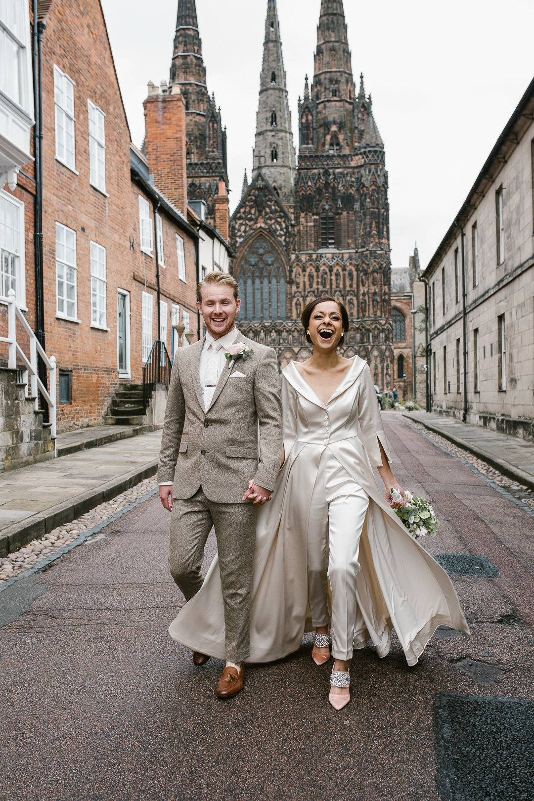 natural happy photo of bride and groom holding hands laughing with lichfield cathedral in the background- lichfield wedding photographer