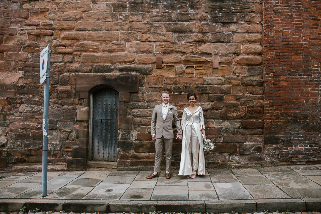 quirky photo of bride and groom standing in front of a brick wall in lichfield after their intimate wedding- lichfield wedding 