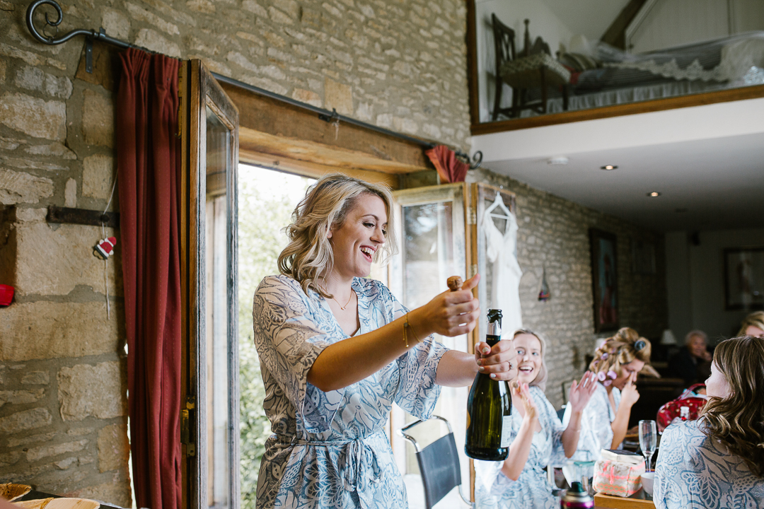 bride popping open the champagne on the morning of her wedding