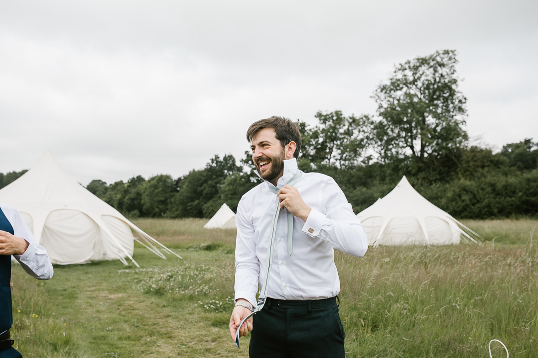 groom getting dressed for his wedding outdoors at his summer wedding in the cotswolds