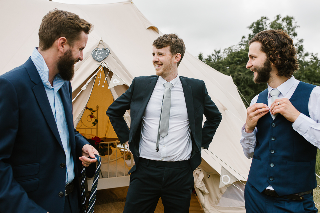 groomsmen tying their ties as they get ready for the outdoor wedding after an evening of glamping 
