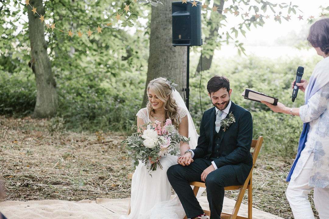 bride and groom laughing during a reading in their woodland outdoor wedding ceremony