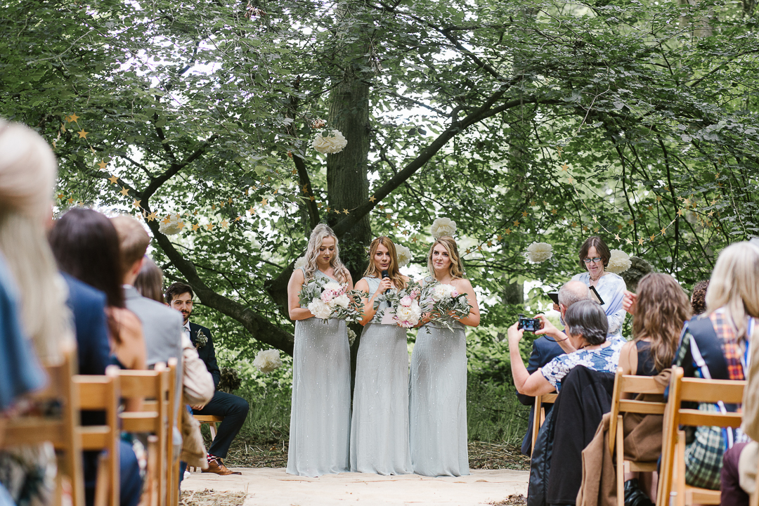 natural photo of bridesmaids doing an emotional reading during an outdoor wedding blessing