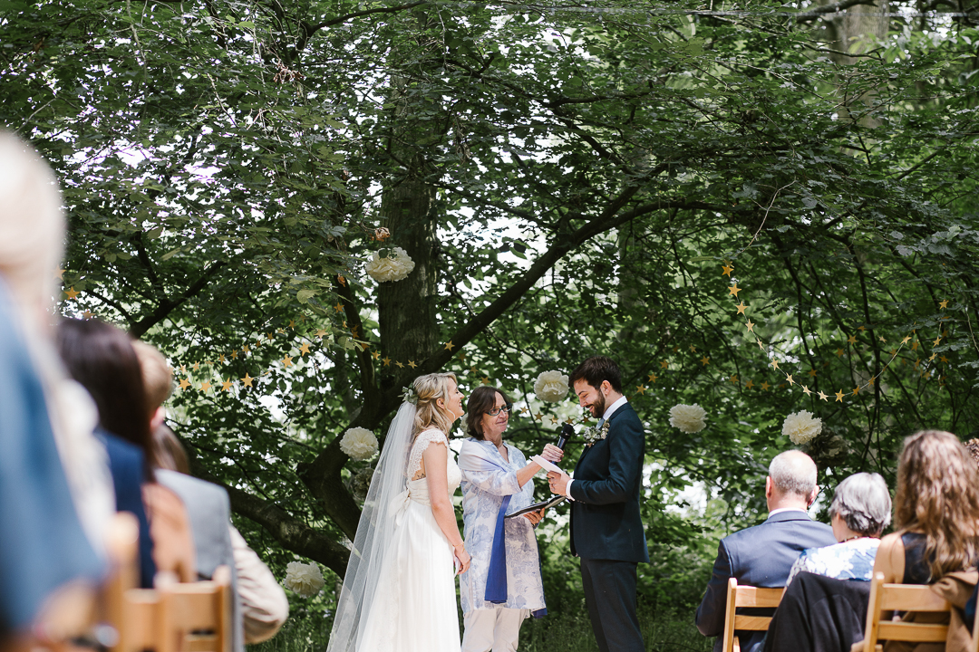 view from down the aisle of bride and groom reading their own vows in woodland wedding in the cotswolds- cotswolds wedding photographer