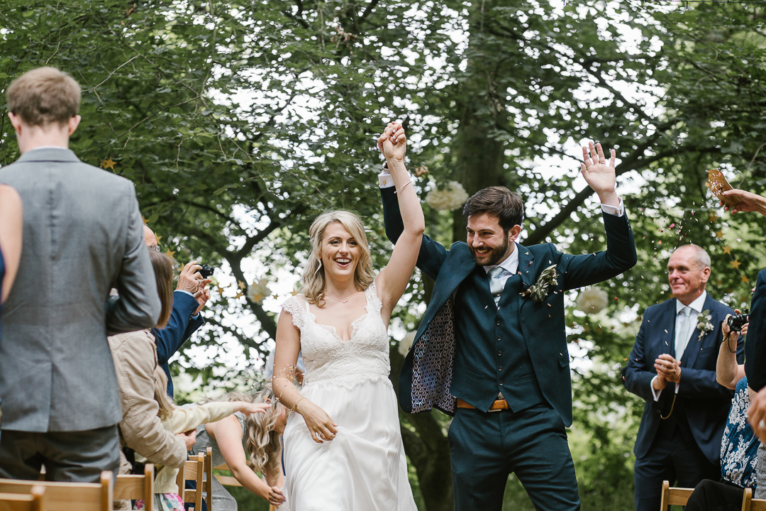 fun photo of the bride and groom waving their hands in the air after becoming husband and wife at their festival wedding in the cotswolds