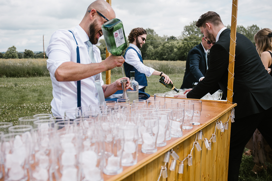 Groomsmen pouring gin into glasses on the DIY wooden bar