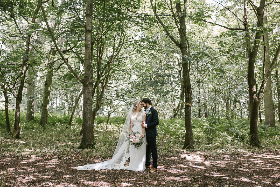 full length photo of bride and groom snuggled up in the forest after their forest wedding