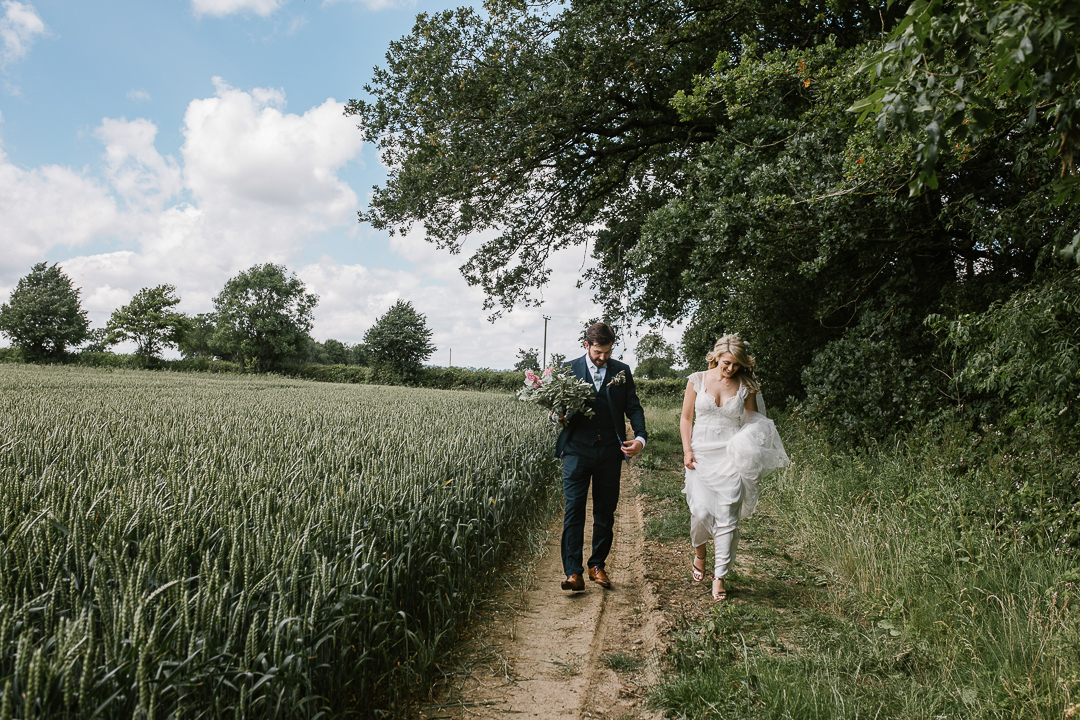 bride and groom walking through a crop field at their festival summer wedding