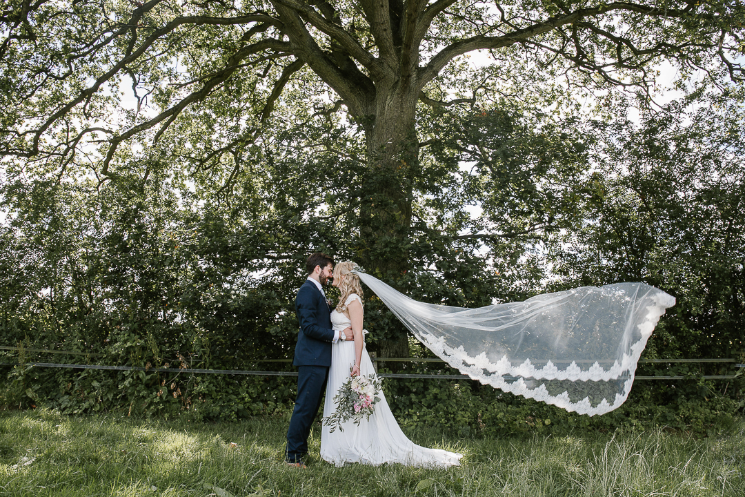 romantic photo of bride and groom kissing in a field with the brides long veil blowing through the air 
