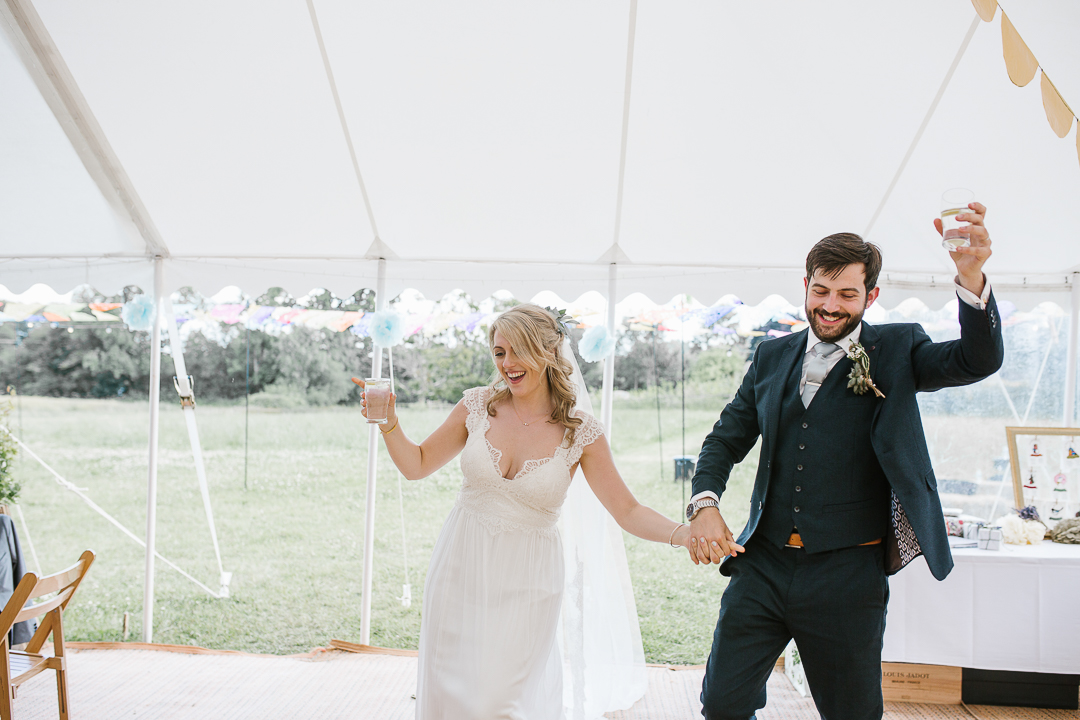 fun photo of bride and groom entering their festival themed marquee wedding venue- cotswolds wedding photography 