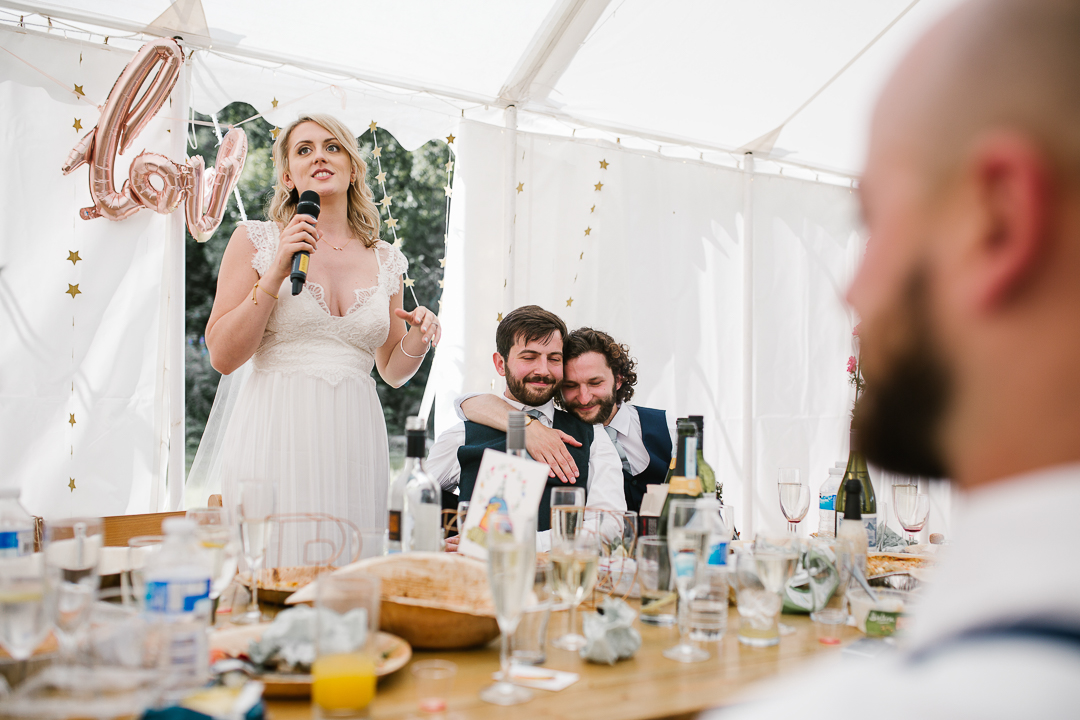 emotional photo of bride doing a bride speech while the groom cries with his best man