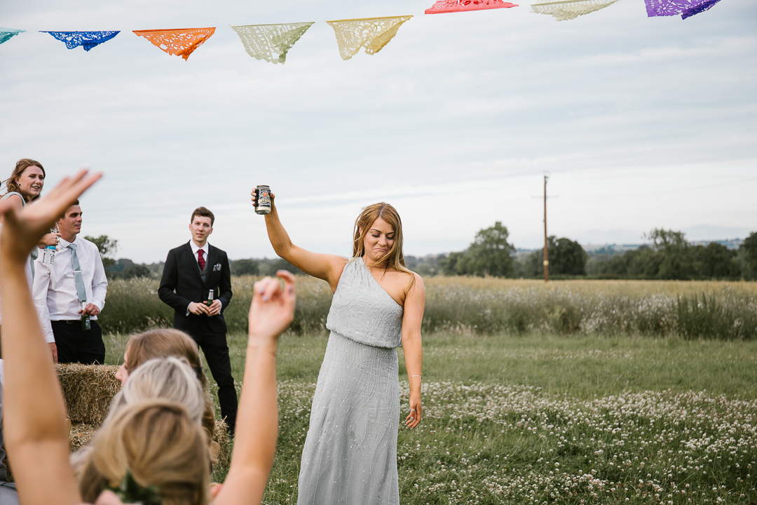 bridesmaid holding cider in hand cheering the wedding guests at the outdoor wedding 
