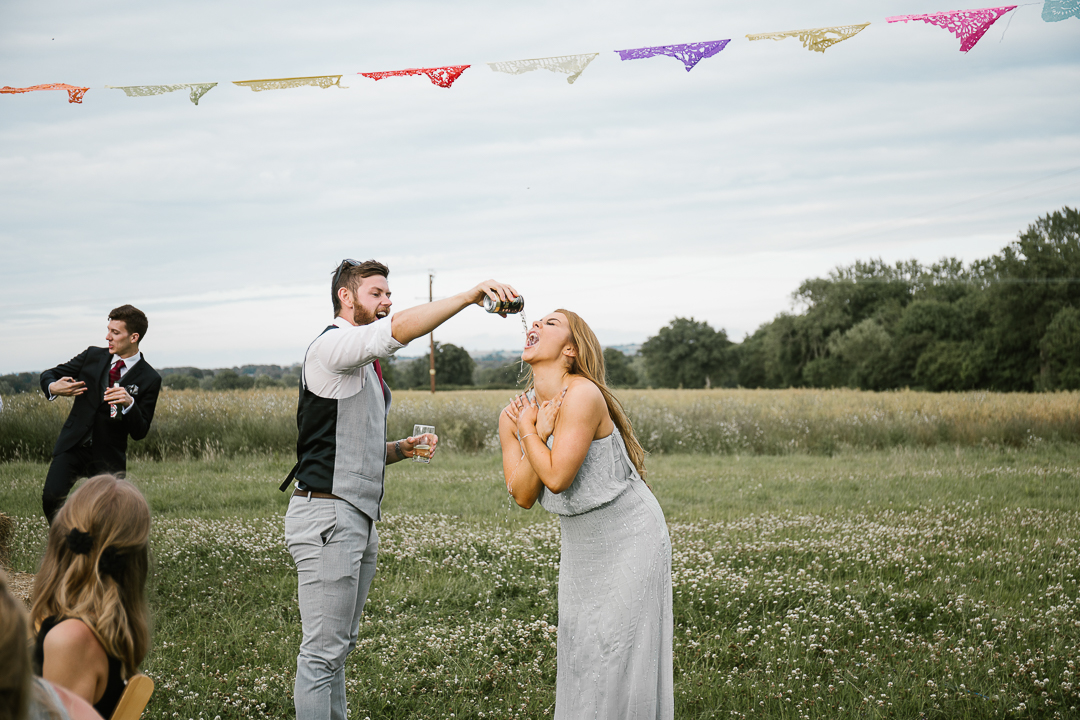 bridesmaid having cider poured down her face as she parties at festival wedding in the cotswolds