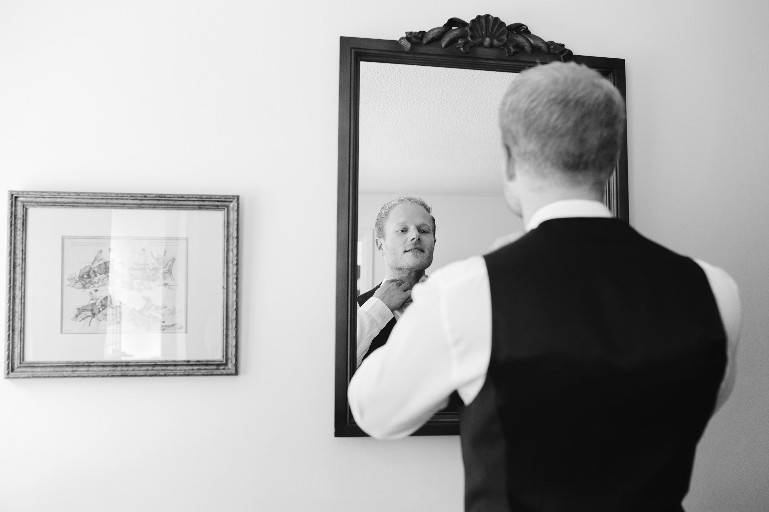 black and white photo of groom tying his bow tie on the morning of his outdoor wedding