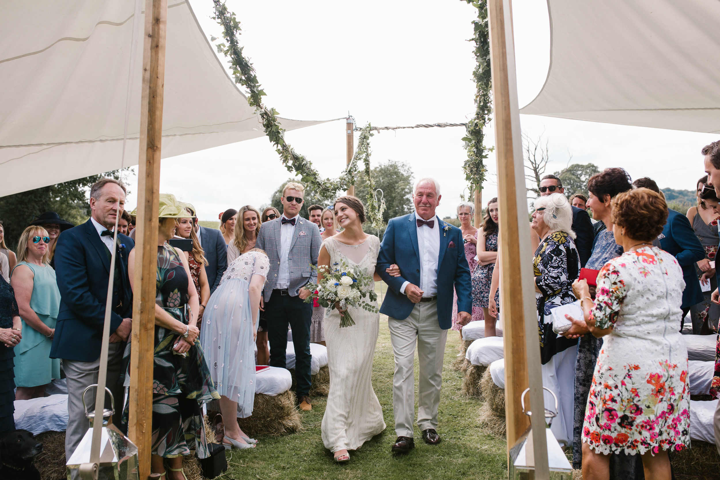 natural photo of bride and father of the bride walking down the outdoor wedding aisle at boho wedding