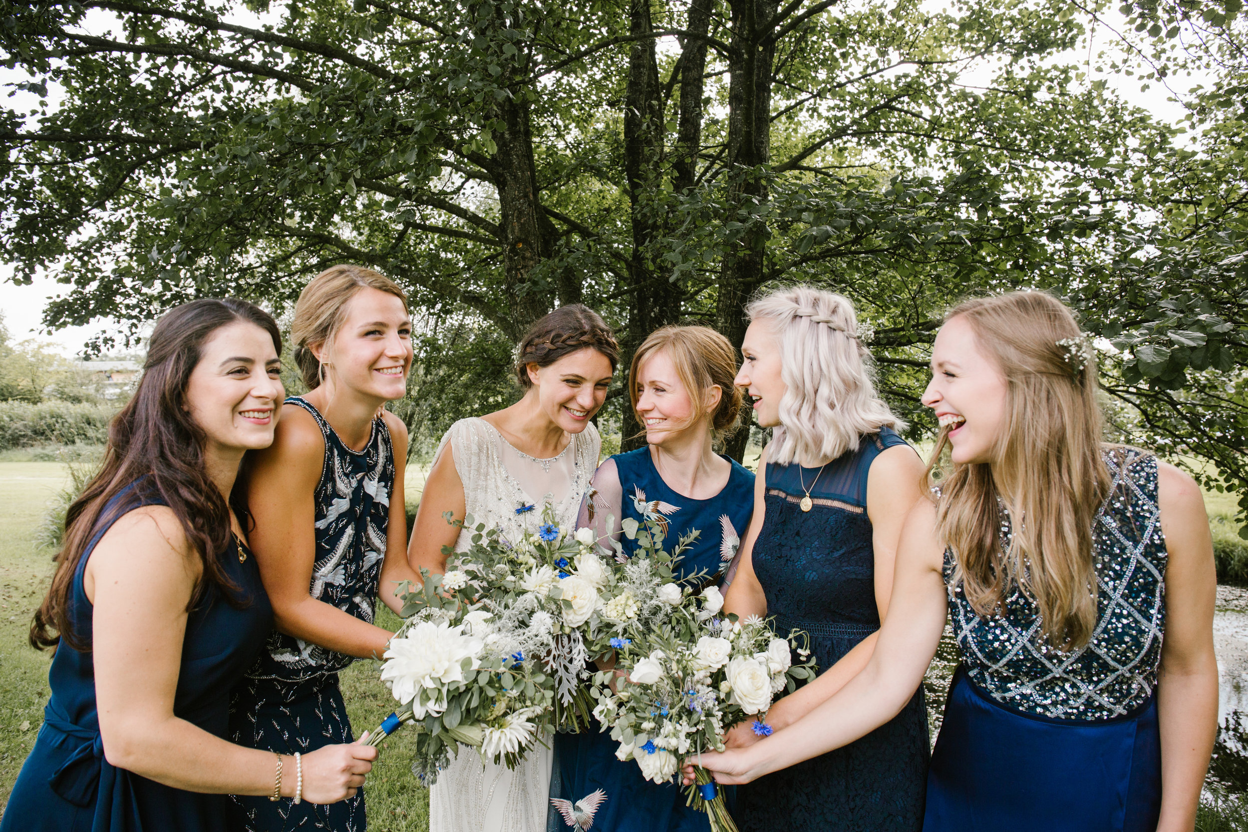 natural photograph of bride with her bridesmaids laughing together after their outdoor wedding ceremony 