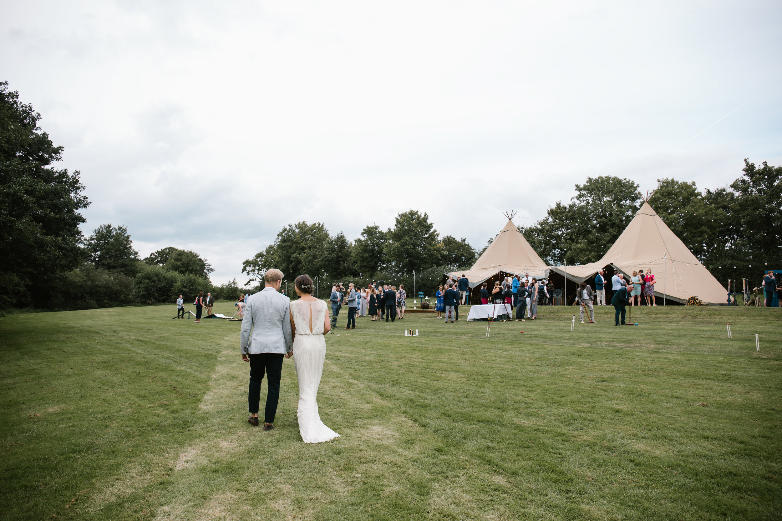 documentary shot of bride and groom walking back to their tipi with all their wedding guests after their outdoor wedding ceremony