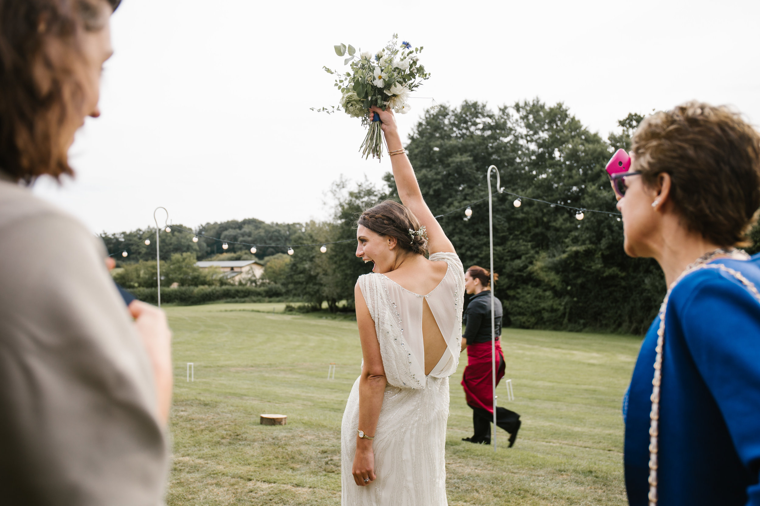 bride celebrating with her flowers high in the air before sitting down for her wedding breakfast