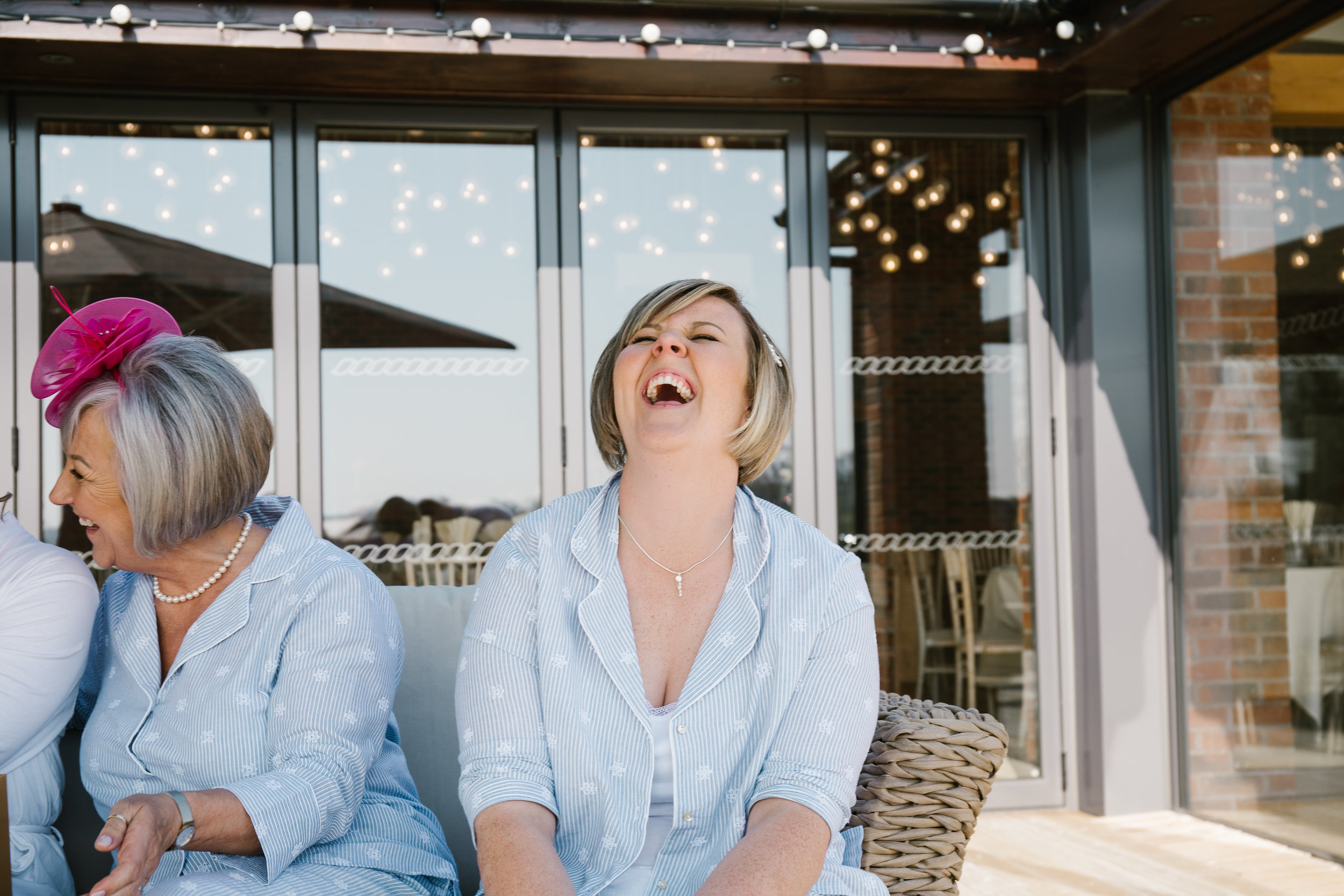 natural photo of bridesmaids laughing while the bride opens gift off groomm