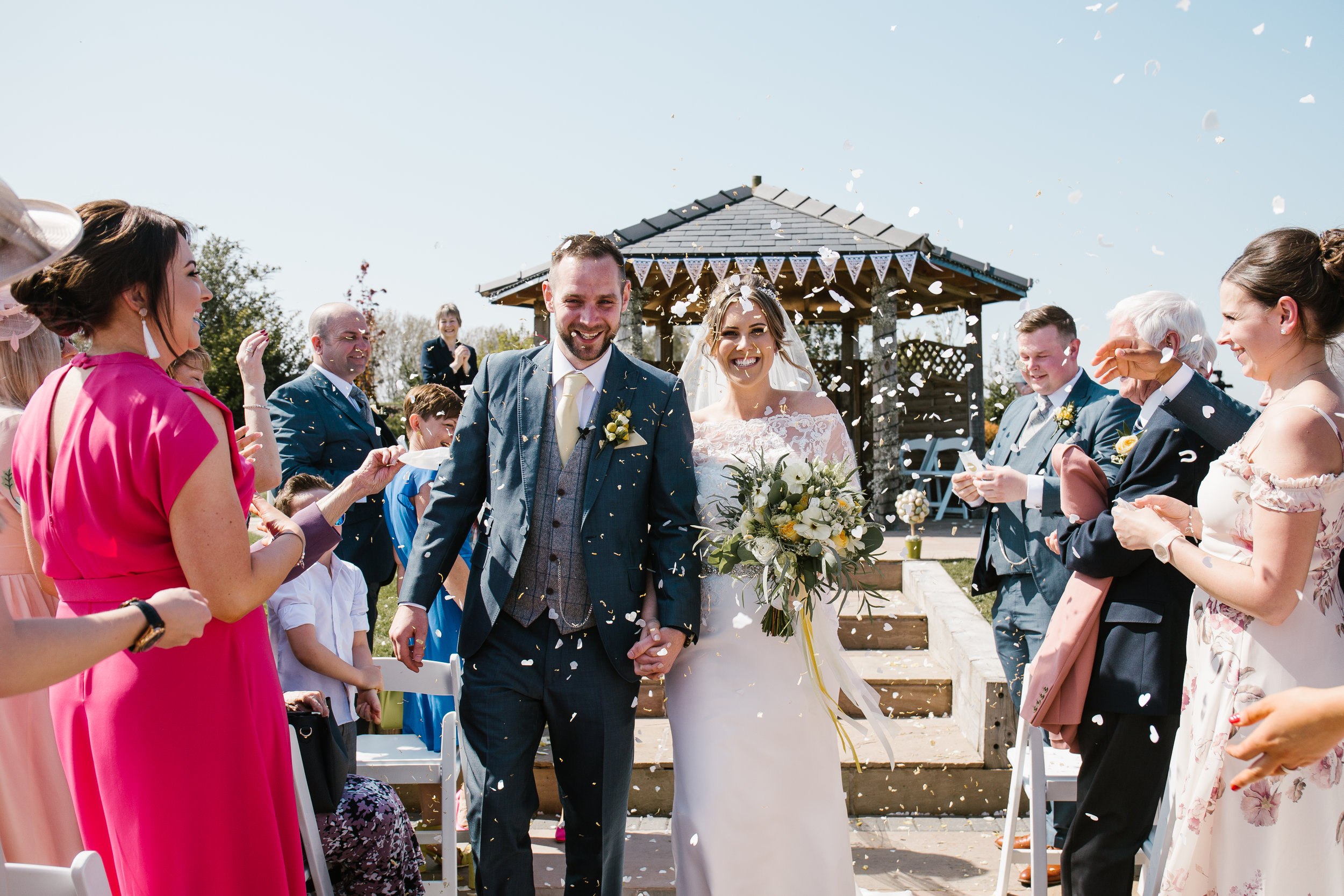 bride and groom laughing together as they walked down the aisle being showered in confetti after becoming husband and wife