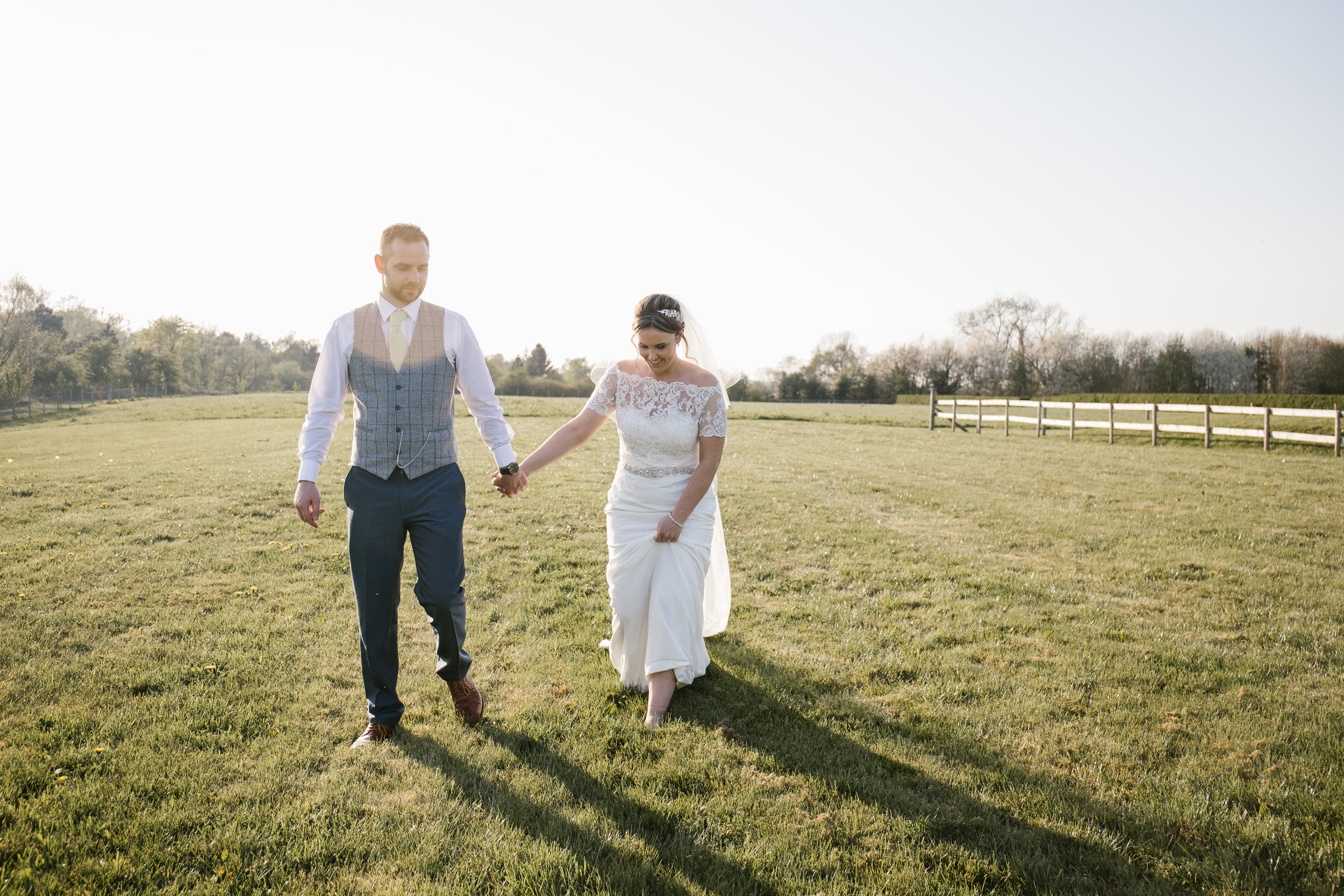 bride and groom walking hand in hand through a field 