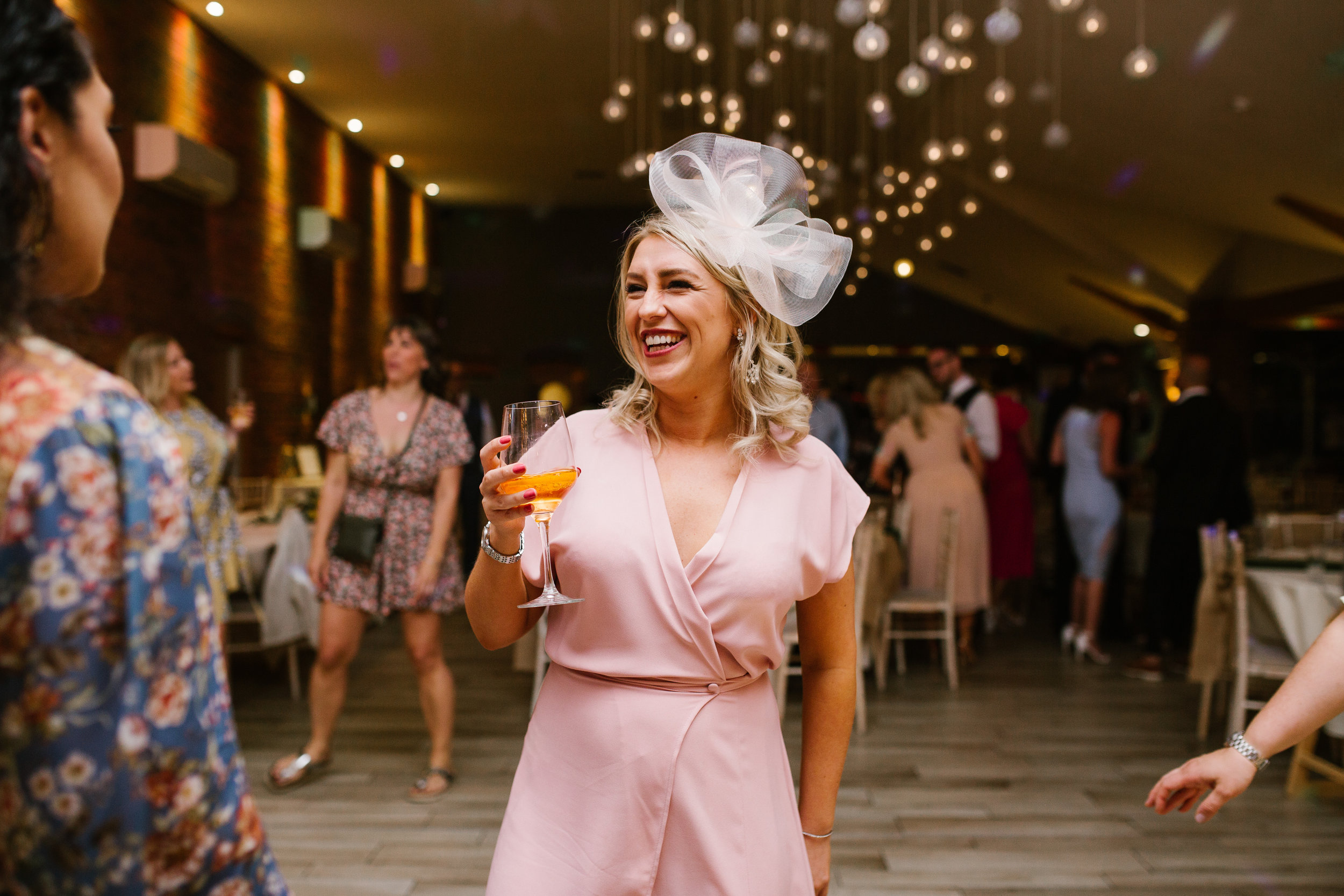 wedding guest dressed in pink holding wine standing on the dance floor smiling