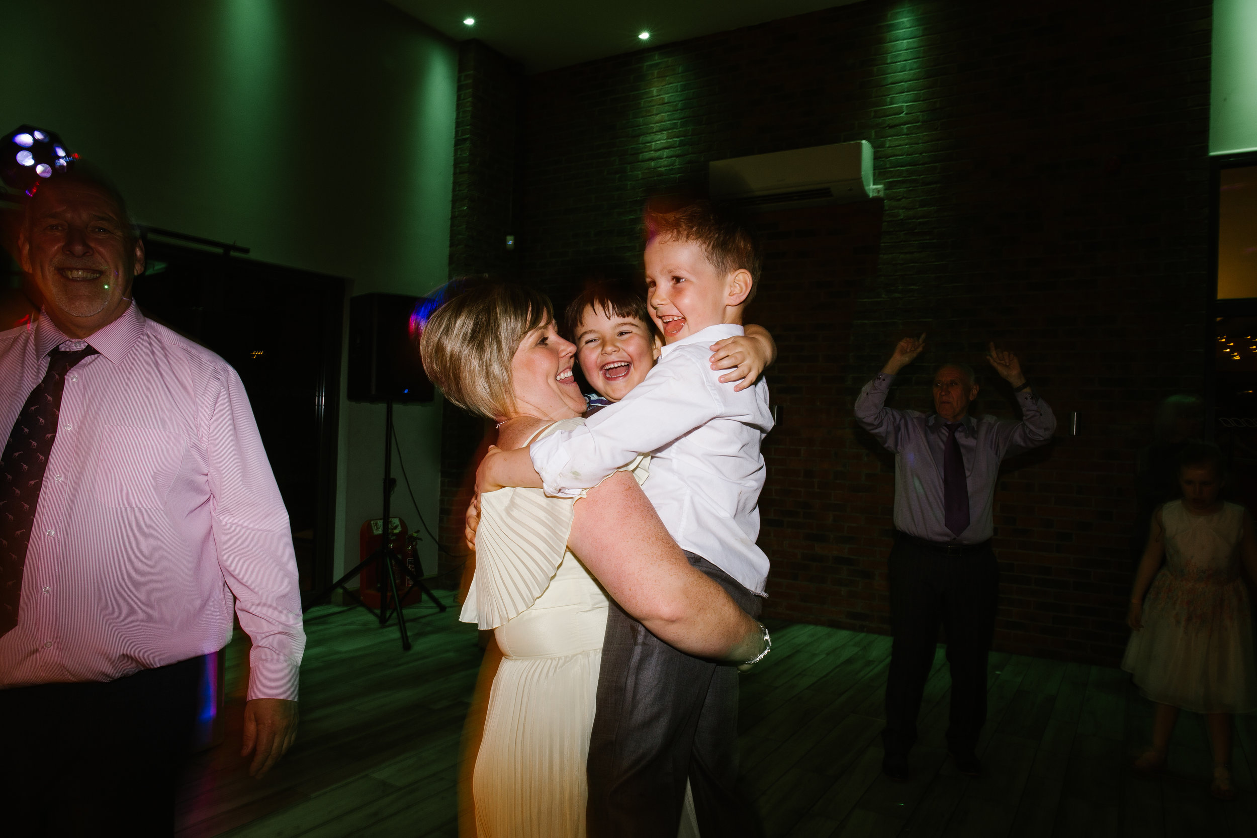 bridesmaid holding two small children as they laugh and dance together on the dance floor