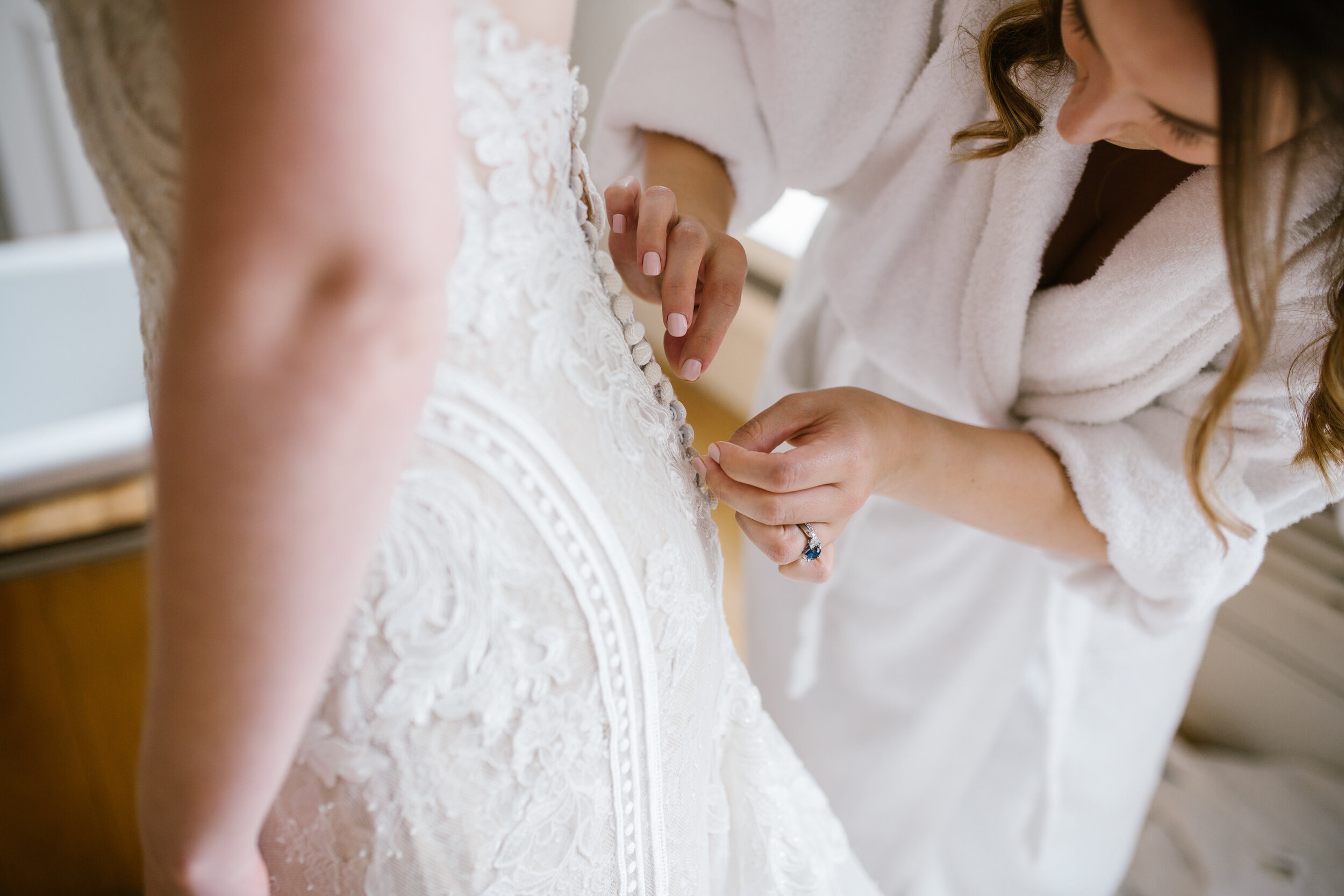 Bridesmaid buttoning up the angelica bridal lace gown up 