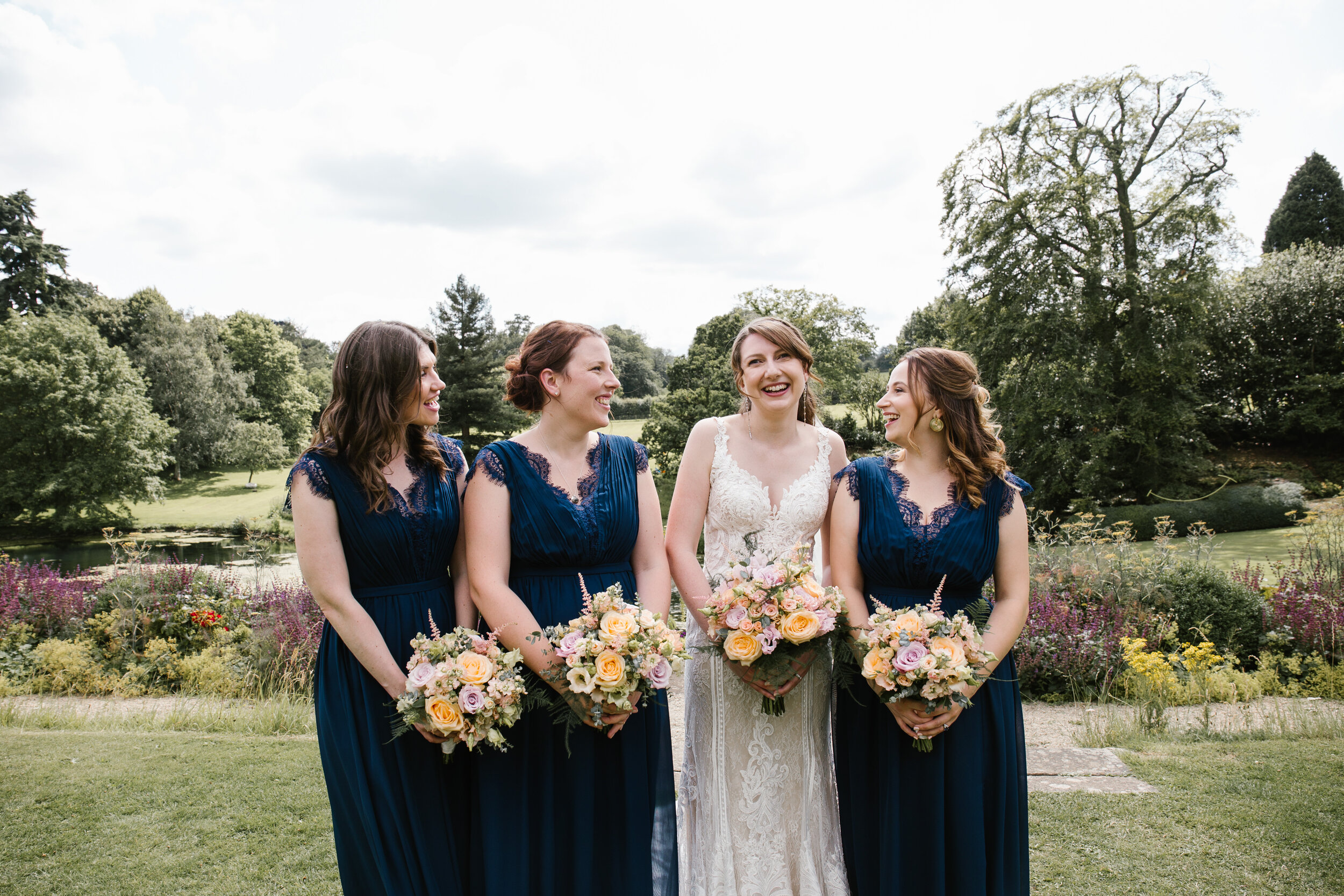 natural photo of bride with her bridesmaids in the beautiful summer grounds of cowley manor