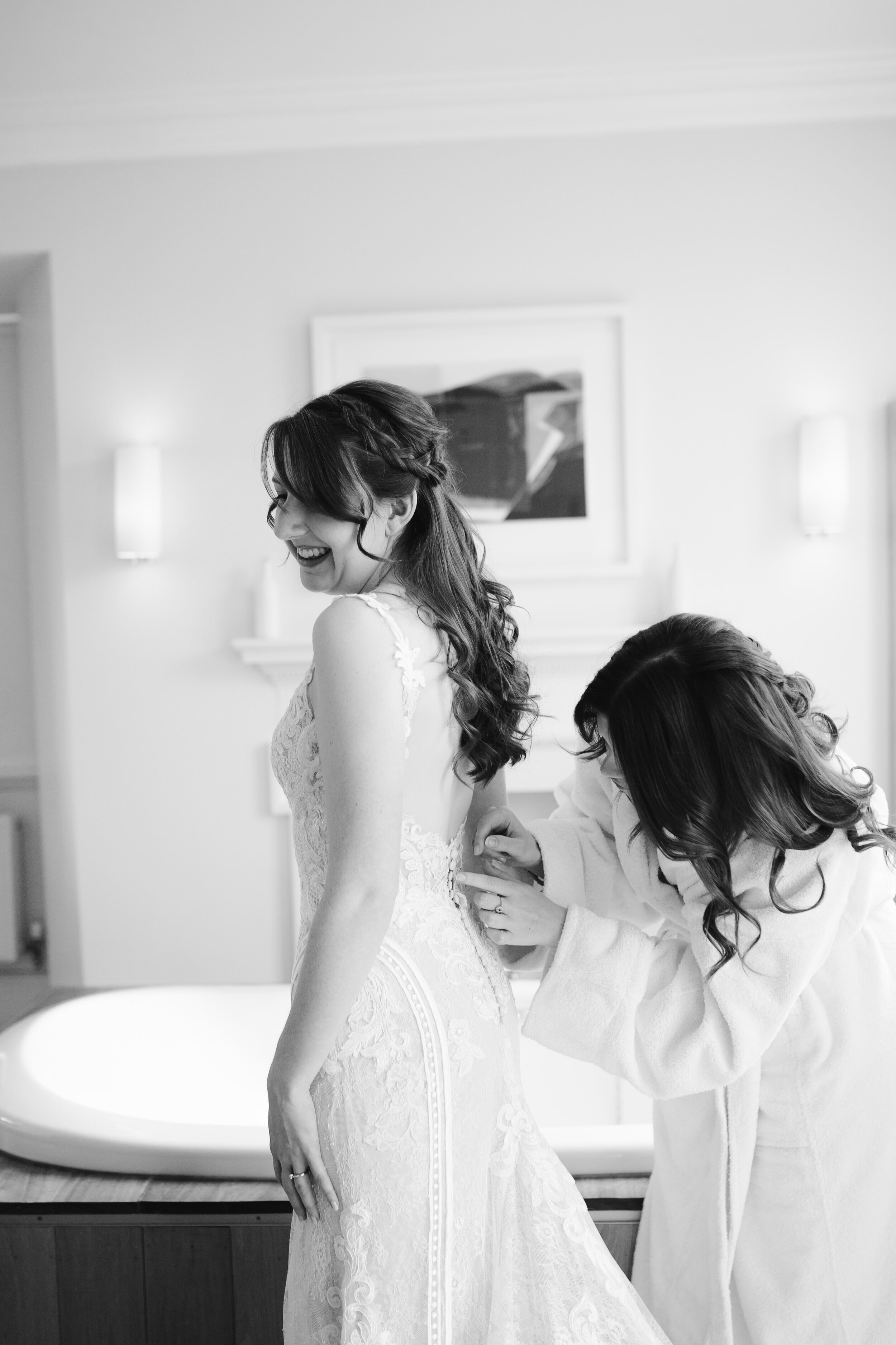 black and white photo of bridesmaid doing last minute touches and buttoning up the lace bridal gown