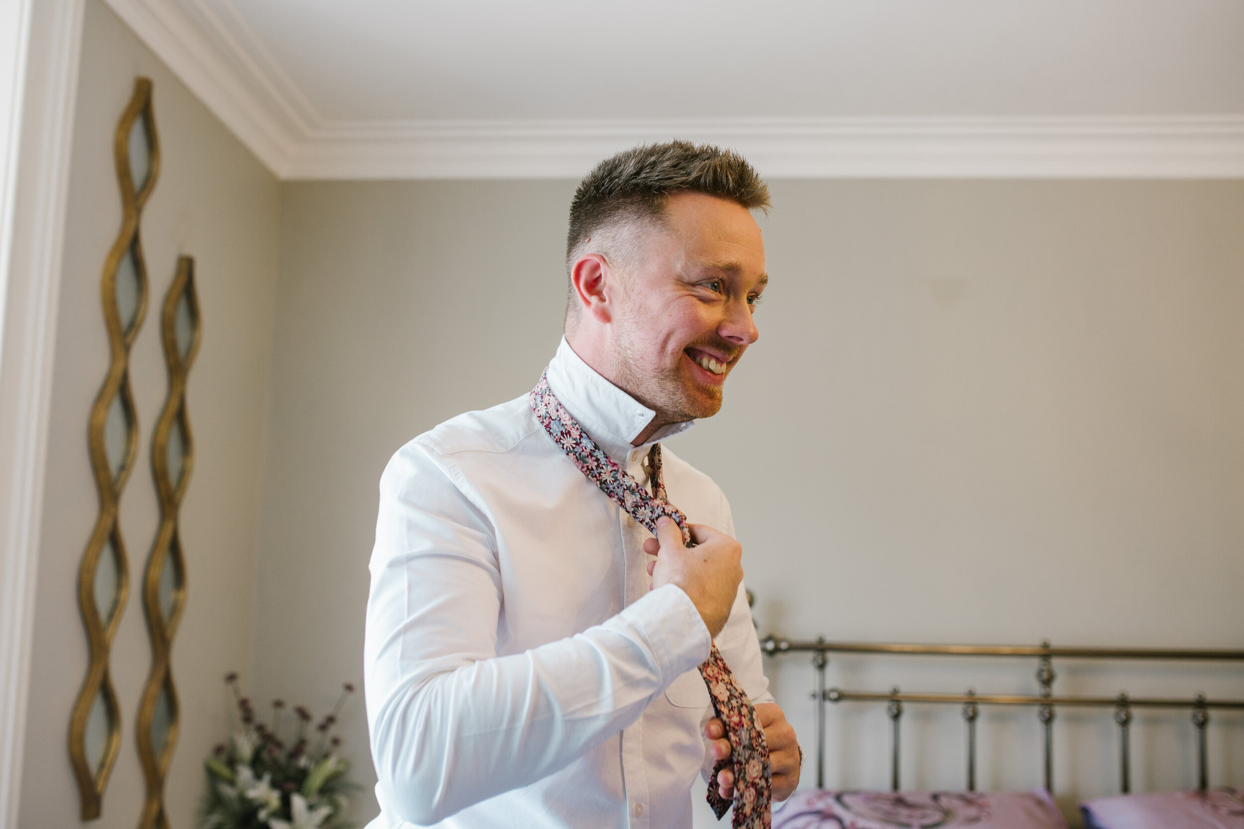 natural photo of groom putting on his tie on the morning of his wedding