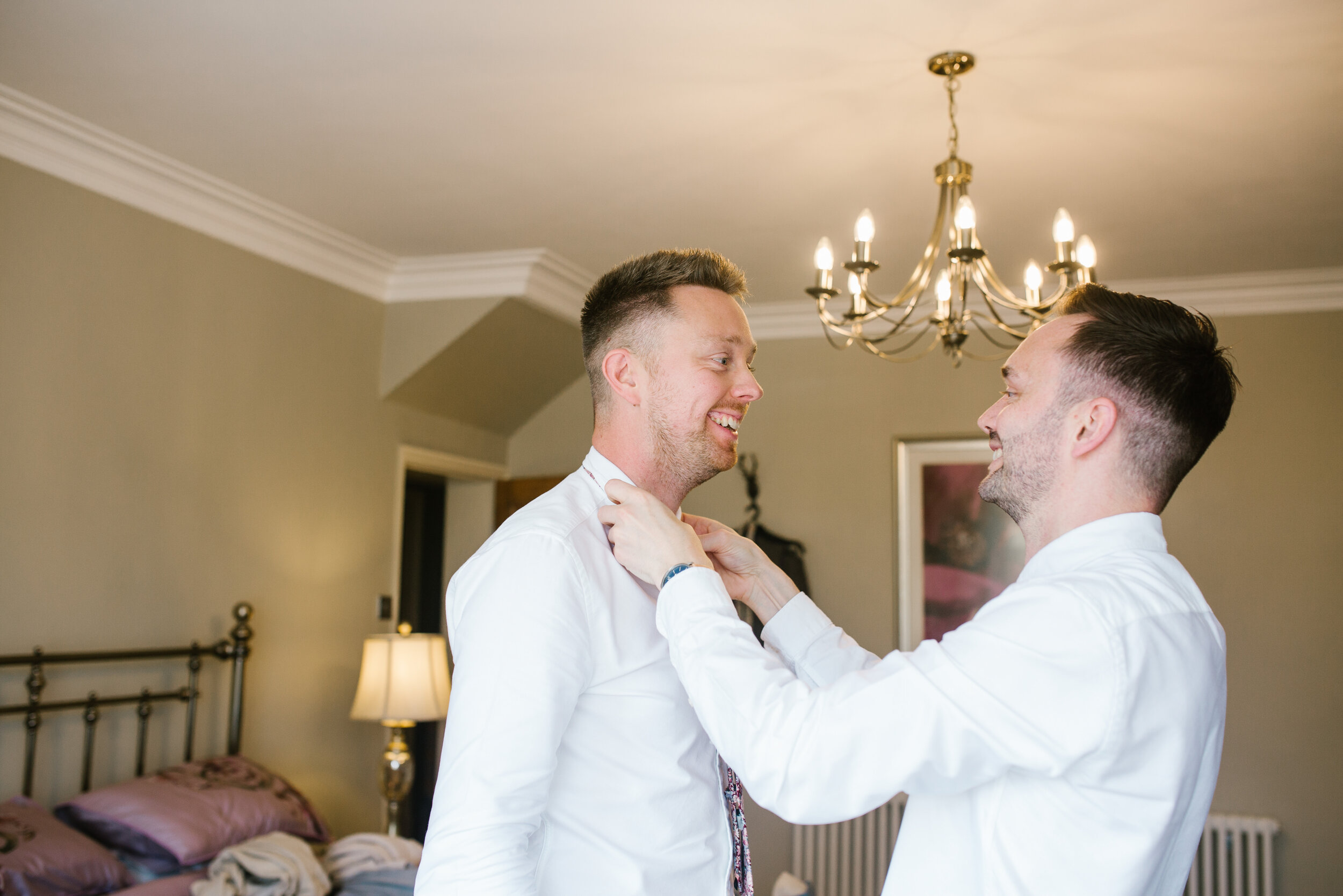 bright fun photo of the two grooms getting each other ready on the morning of their wedding day