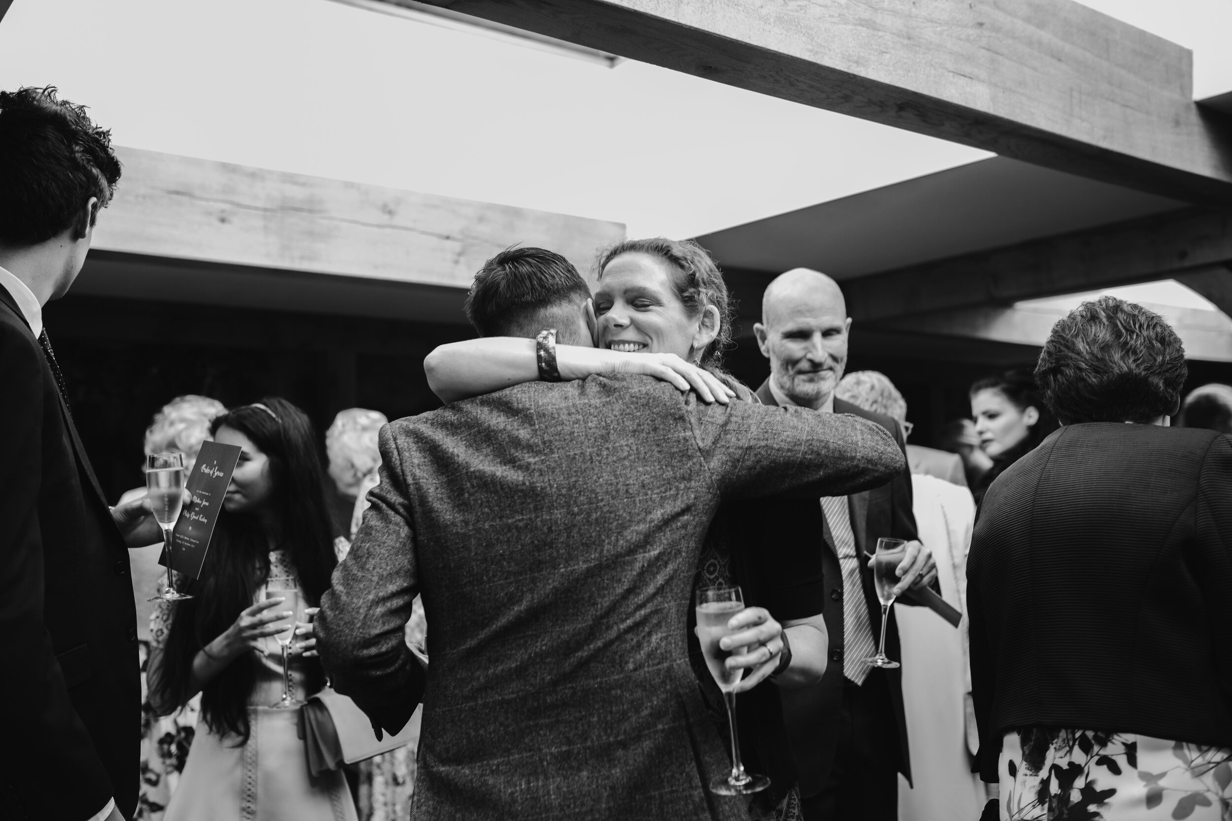 black and white candid photo of a guest hugging the groom after the ceremony