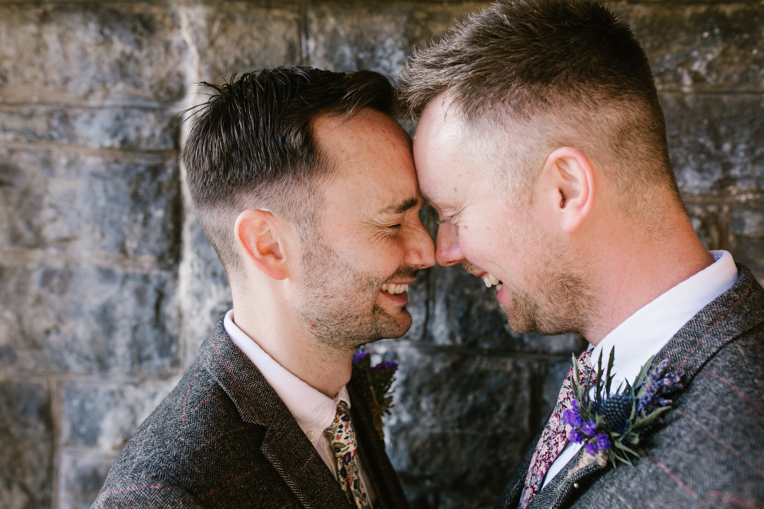 an intimate up close photo of two grooms smiling together with their faces touching