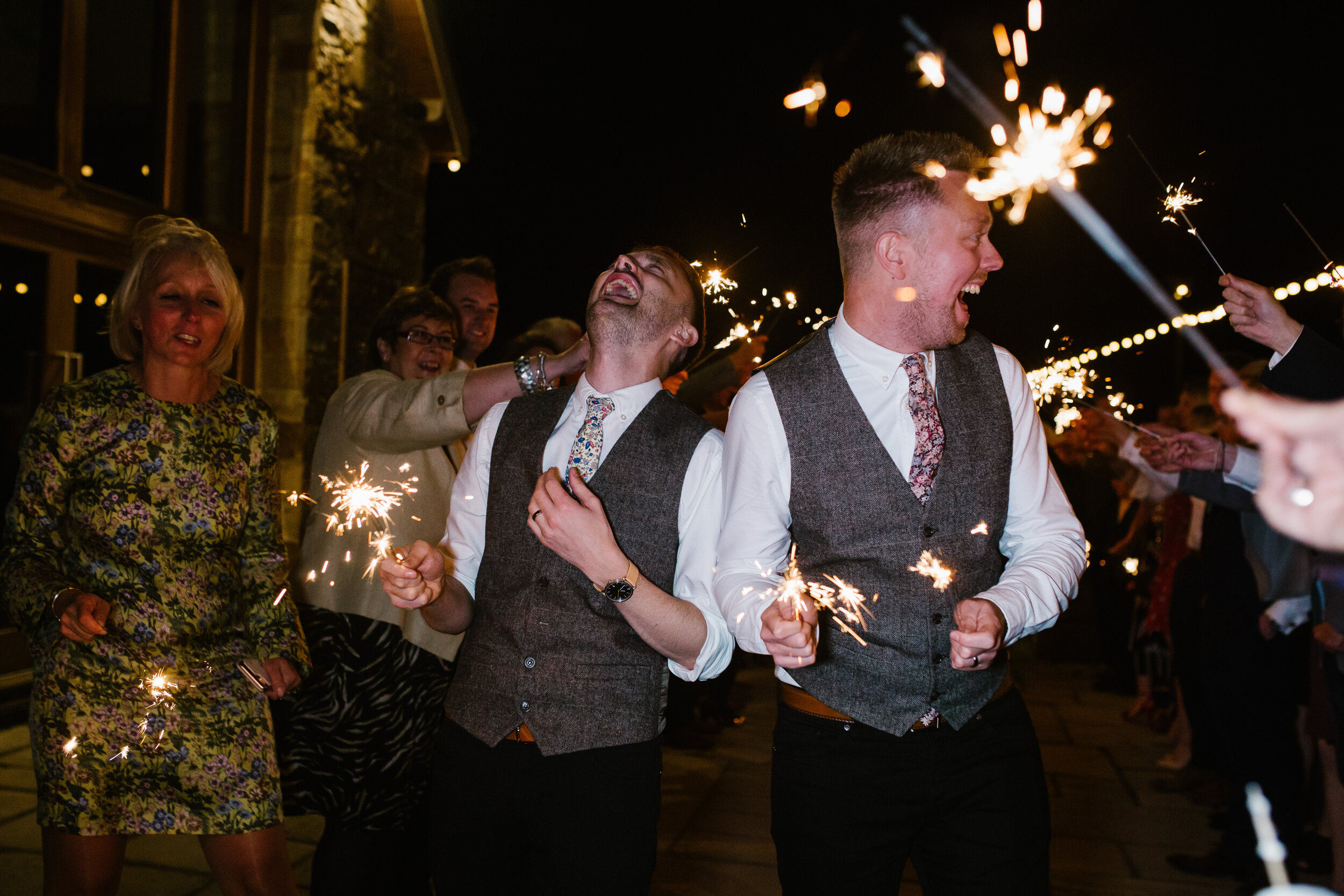 grooms laughing with sparklers at the end of their wedding