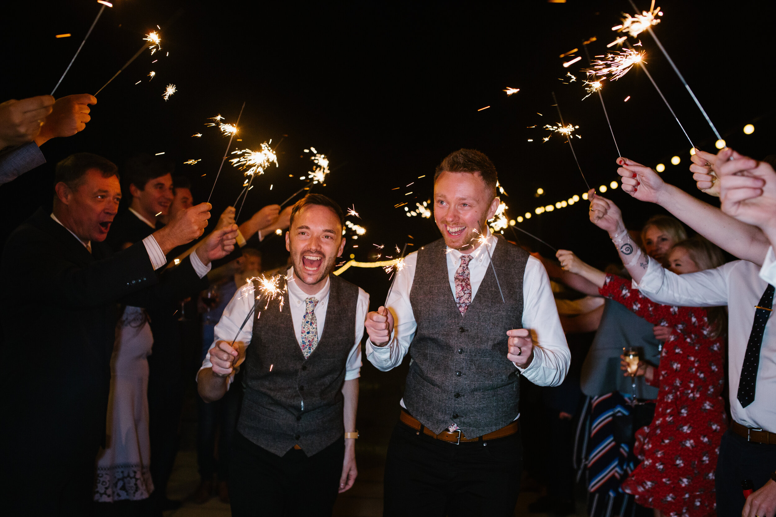 natural photo of grooms walking with sparklers
