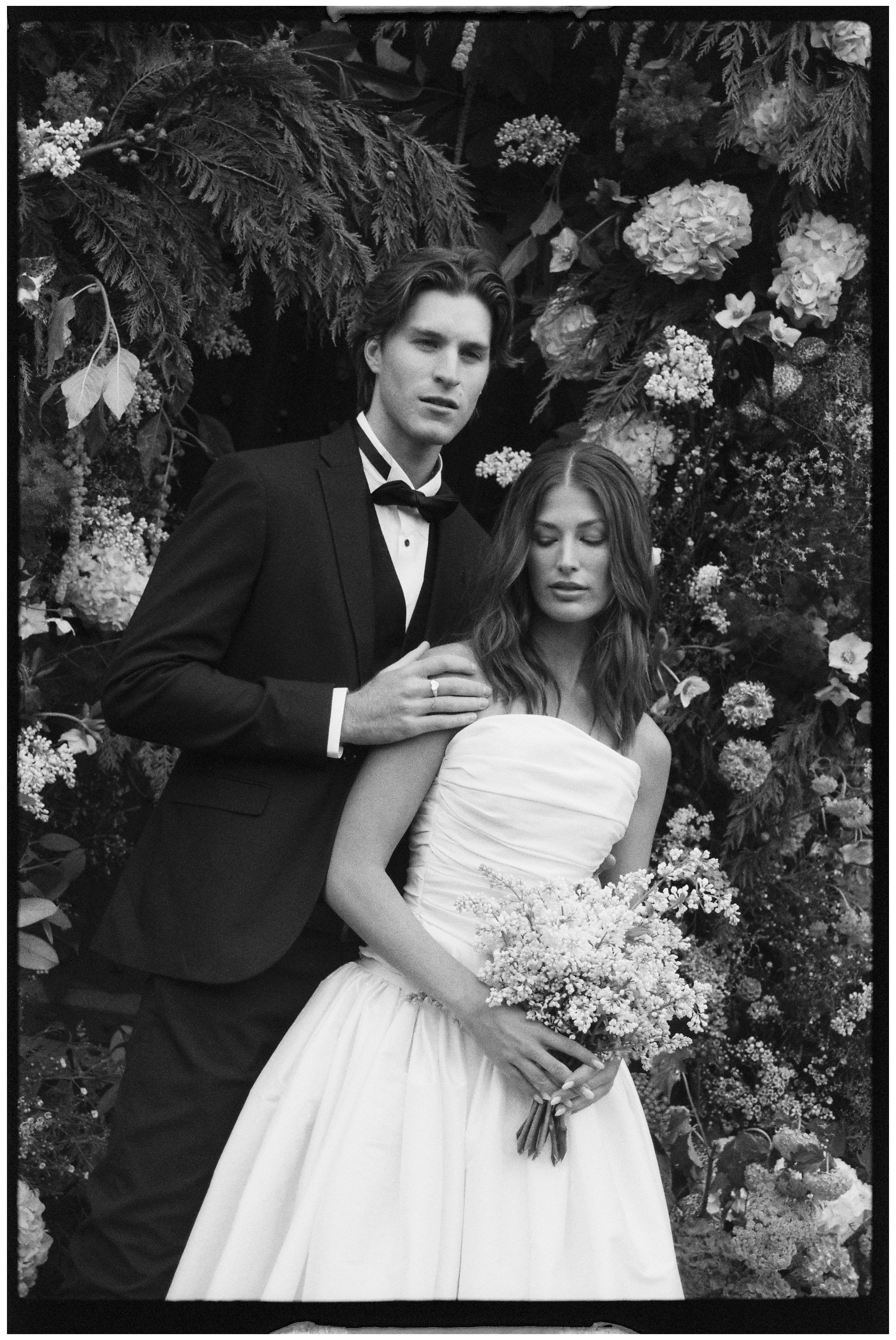 Black and white photo of Bride and Groom stood surrounded by flowers