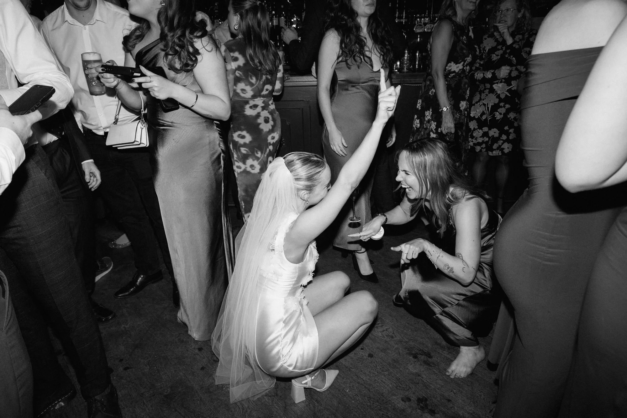 Black and white photo of bride and brisesmaid crouched down on the dancefloor at Balfour St Barts in London