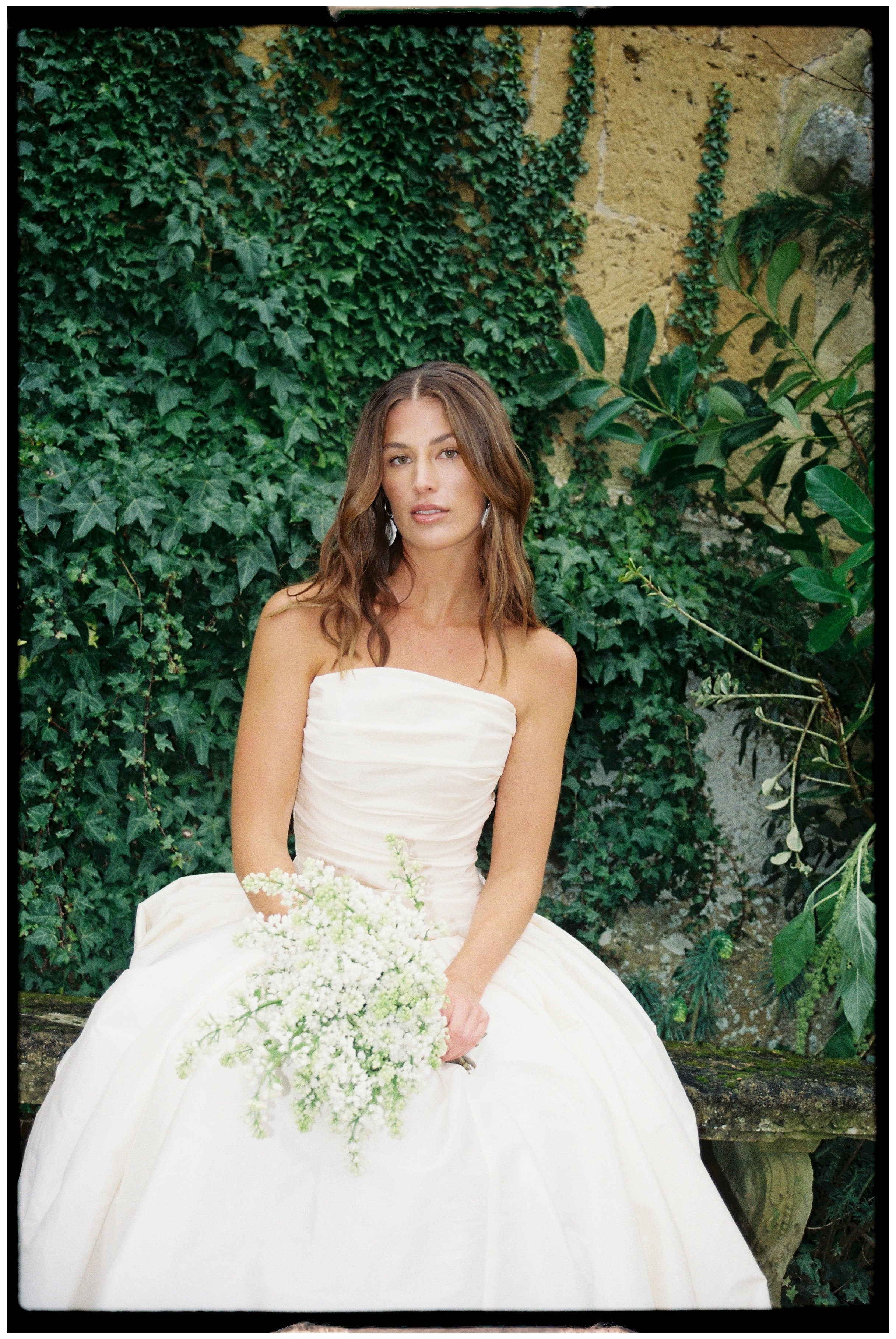 Bridal portrait of a bride sat down looking at the camera holding onto her bouquet