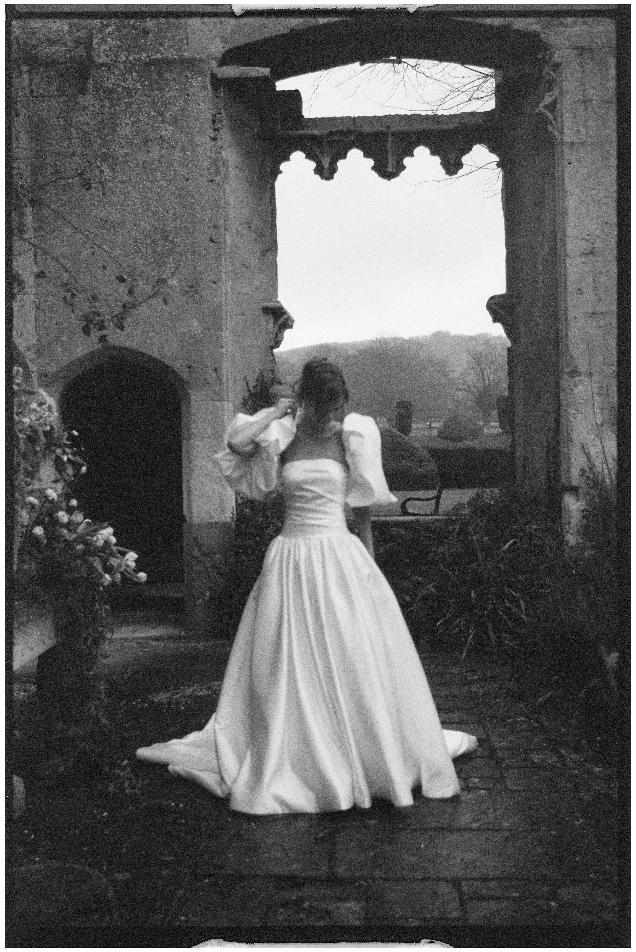 Blurry black and white film portrait of a bride stood in the grounds of Sudeley Castle