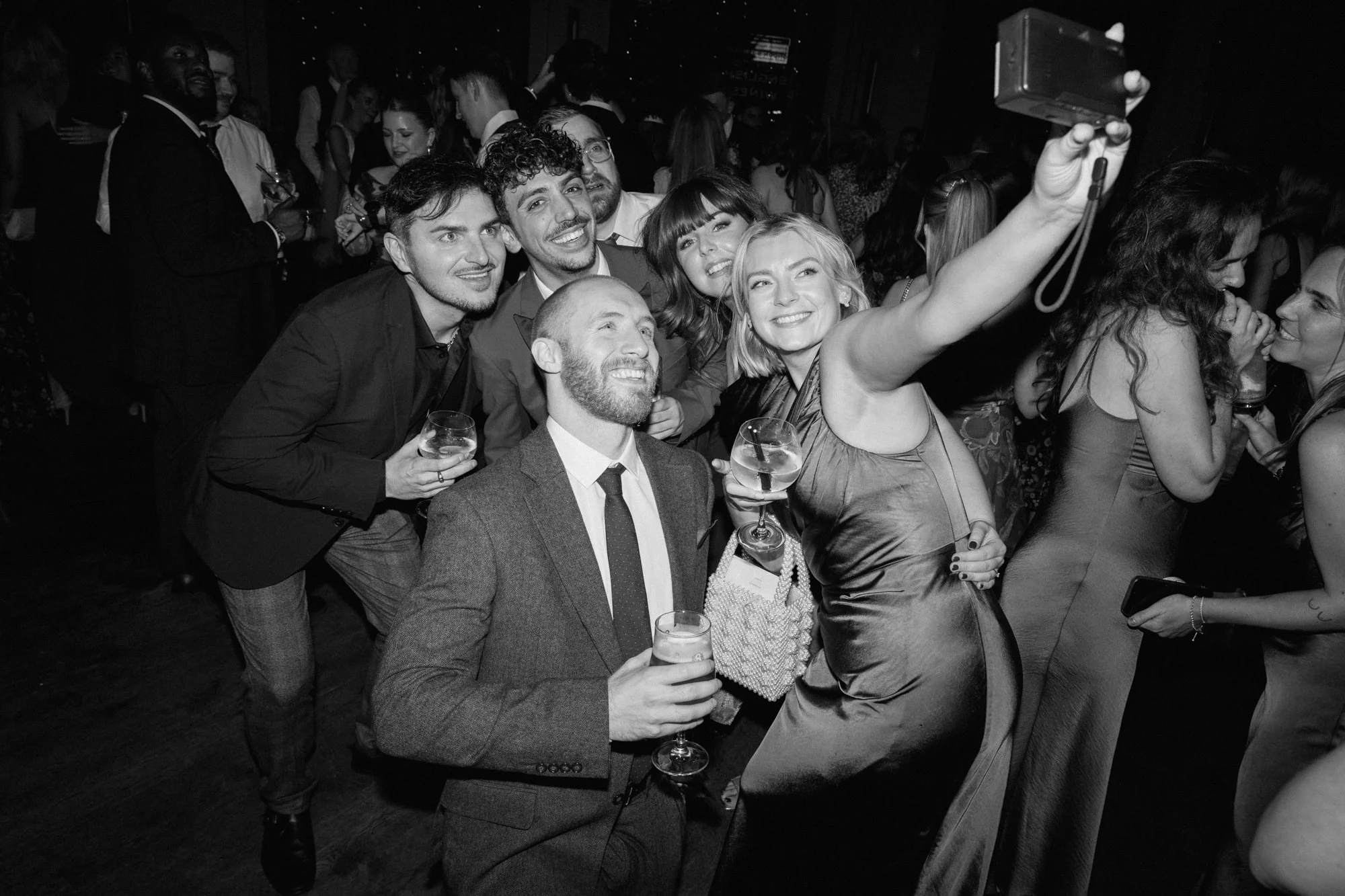 Black and white photo of wedding guets on the dancefloor taking a photo on a disposable camera
