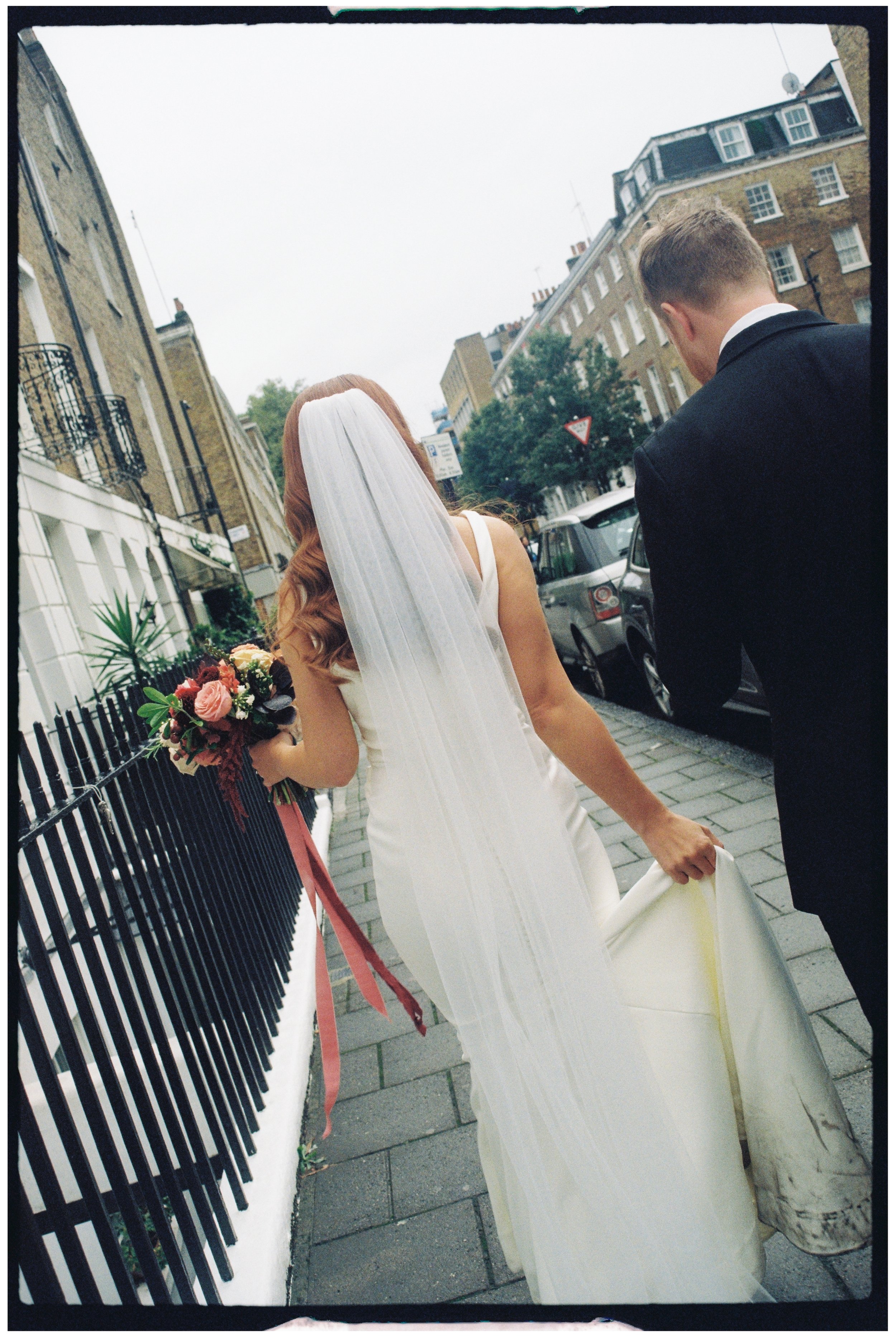 The back of a bride and groom on 35mm as they walk down the street together in London