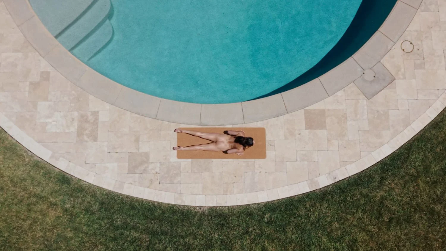 top down view of a lady doing naked yoga in upward dog by a circular pool