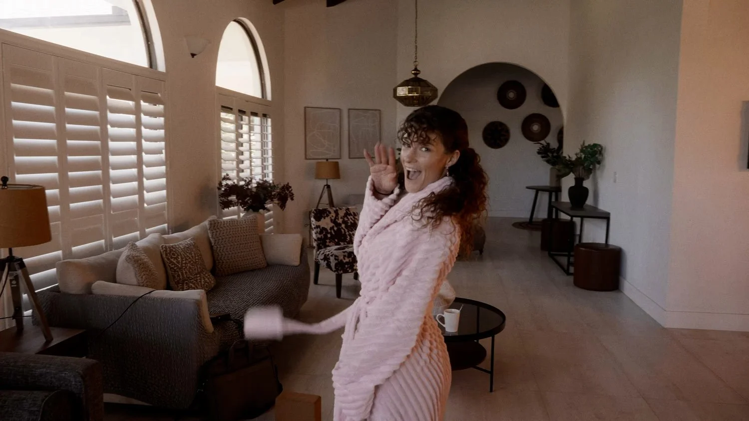 woman in a pink robe waving and smiling at camera