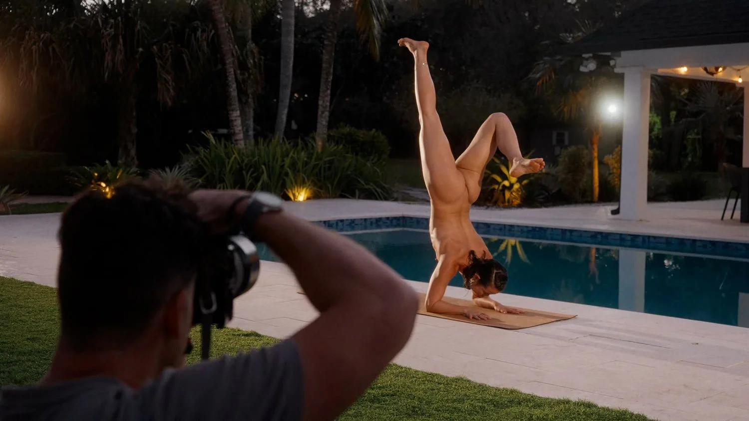 naked woman doing a forearm stand on yoga mat with photographer taking a photo