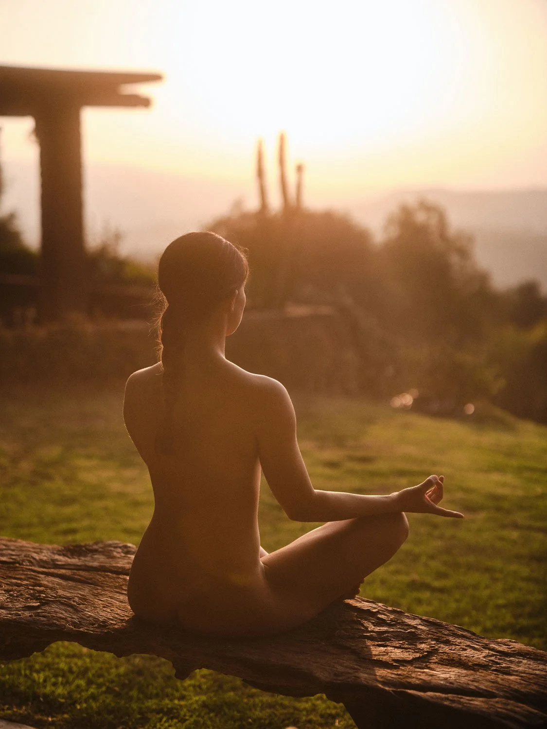 woman practicing naked meditation outside during sunset