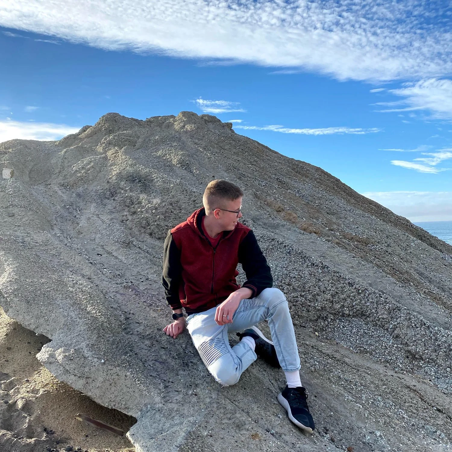 man sitting on the side of a mountain with blue sky in the background