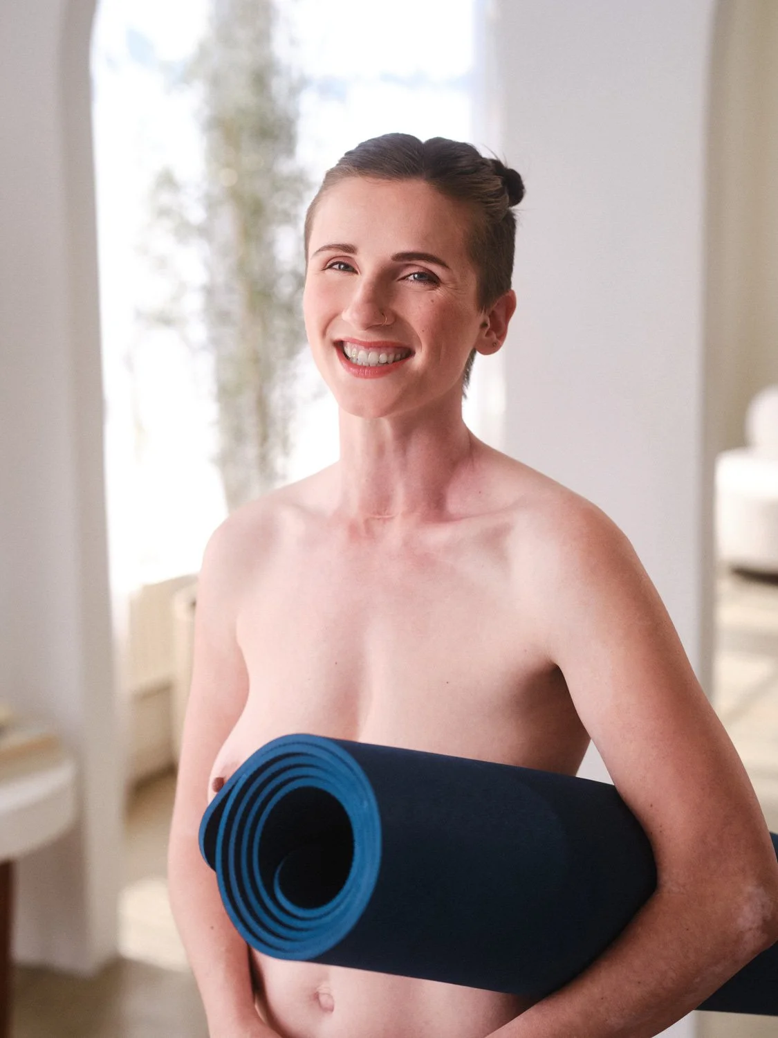smiling naked woman holding a blue rolled yoga mat