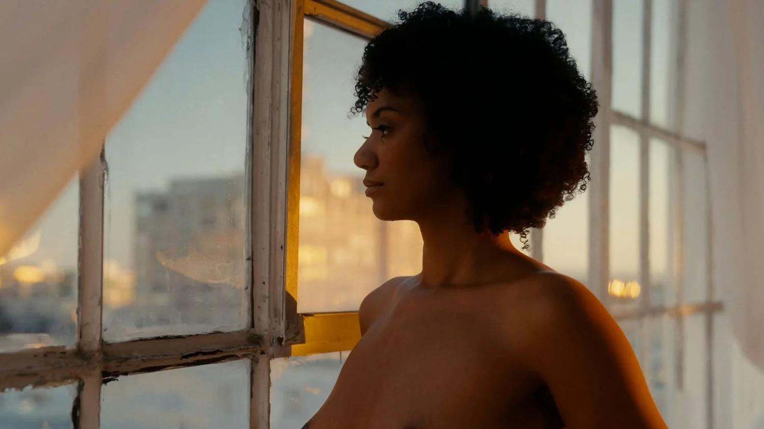 nude woman starting out window during golden hour sunset